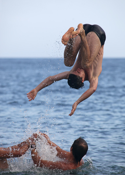 mężczyzna znajomych, grając w morzu, jeden wykonywania Salto - Zdjęcie, obraz