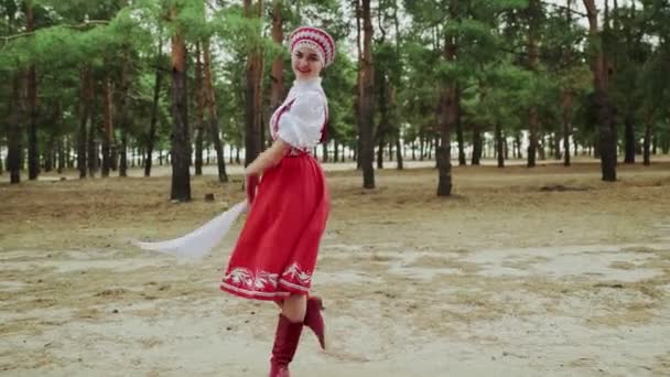 Красивая женщина в красном русском традиционном народном костюме с платком танцует в лесу - Кадры, видео