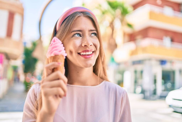 Молодая кавказская девушка улыбается счастливо поедая мороженое в городе. - Фото, изображение
