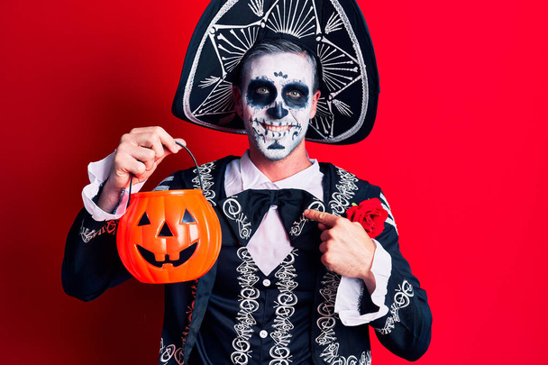 Young man wearing mexican day of the dead costume holding pumpkin pointing finger to one self smiling happy and proud  - Φωτογραφία, εικόνα
