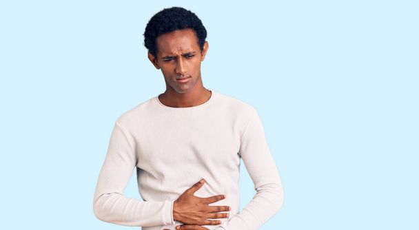 Hombre guapo africano que usa suéter de invierno casual con la mano en el estómago porque la indigestión, la enfermedad dolorosa sensación de malestar. concepto ache.  - Foto, imagen