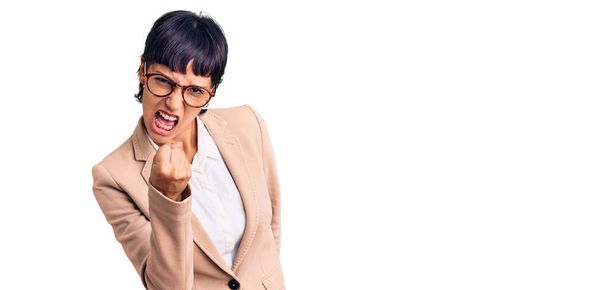 Young brunette woman with short hair wearing business jacket and glasses angry and mad raising fist frustrated and furious while shouting with anger. rage and aggressive concept.  - Photo, Image
