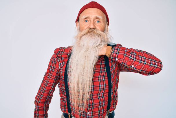 Старий старший чоловік з сірим волоссям і довгою бородою, одягнений в хіпстерський вигляд з вовняною шапочкою, що розрізає горло рукою як ніж, загрожує агресії з лютим насильством
  - Фото, зображення