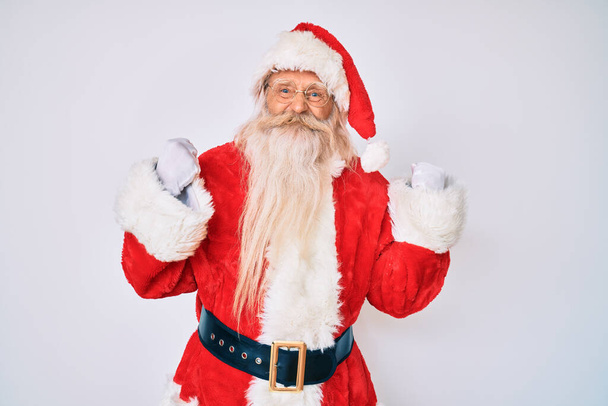 Alter älterer Mann mit grauen Haaren und langem Bart im Weihnachtsmann-Kostüm mit Strapsen, die vor Erfolg nur so strotzen, die Arme in die Höhe gereckt und die Augen geschlossen, um den Sieg lächelnd zu feiern. Siegerkonzept.  - Foto, Bild