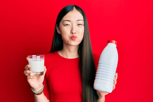 Μια νεαρή Κινέζα πίνει ένα ποτήρι φρέσκο γάλα φουσκώνοντας μάγουλα με αστείο πρόσωπο. στόμα φουσκωμένο με αέρα, που πιάνει αέρα.  - Φωτογραφία, εικόνα