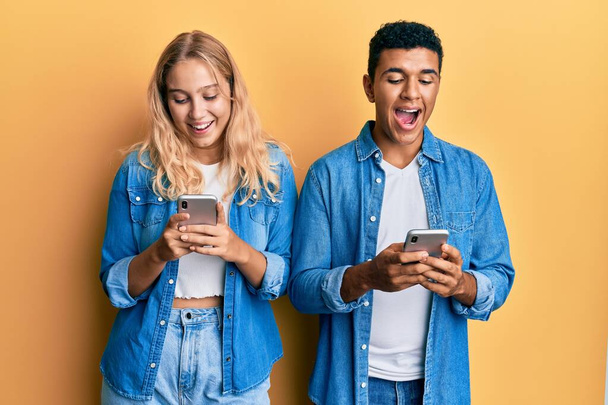 Young interracial couple using smartphone celebrating crazy and amazed for success with open eyes screaming excited.  - Zdjęcie, obraz
