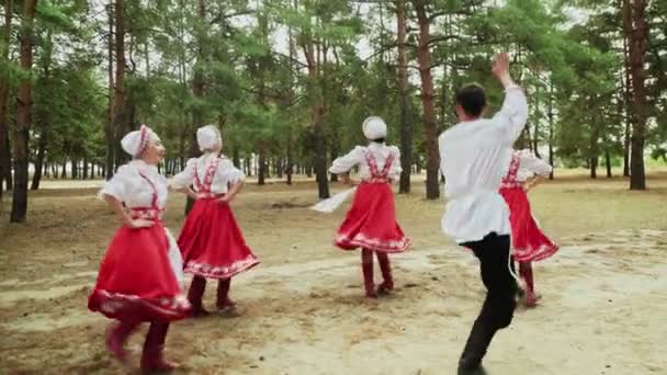 Танцевальная группа танцует русские традиционные танцы в летнем лесу - Кадры, видео