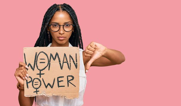 Beautiful hispanic woman holding woman power banner with angry face, negative sign showing dislike with thumbs down, rejection concept  - Zdjęcie, obraz