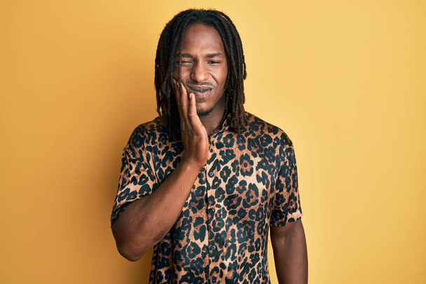 African american man with braids wearing leopard animal print shirt touching mouth with hand with painful expression because of toothache or dental illness on teeth. dentist  - Zdjęcie, obraz
