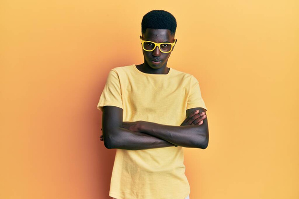 Mladý afroameričan v neformálním oblečení a brýlích skeptický a nervózní, nesouhlasný výraz na tváři se zkříženýma rukama. negativní osoba.  - Fotografie, Obrázek