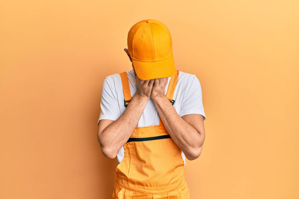 Young hispanic man wearing handyman uniform pointing aside worried and nervous with forefinger, concerned and surprised expression  - Photo, Image