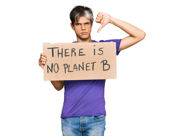 若いヒスパニック系の男が怒っている顔をした惑星Bのバナーはありません保持,親指で嫌いな負の記号を示す下,拒絶概念  - 写真・画像