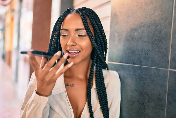 若いアフリカ系アメリカ人女性が笑顔で市内のスマートフォンを使って音声メッセージを送る. - 写真・画像