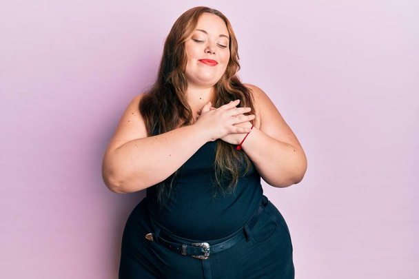 Plus size caucasian young woman wearing casual clothes over pink background smiling with hands on chest, eyes closed with grateful gesture on face. health concept.  - Foto, immagini