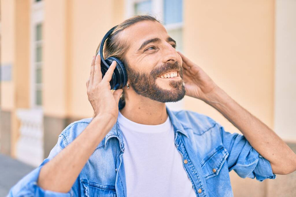 Jovem homem do Oriente Médio sorrindo feliz usando fones de ouvido na cidade. - Foto, Imagem