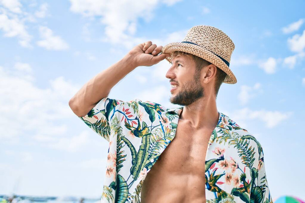 Красива фітнес кавказький чоловік на пляжі в сонячний день в літньому капелюсі
 - Фото, зображення