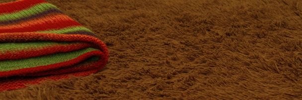 Un plaid tricoté rayé est posé sur une couverture de fourrure marron fourrée avec de longues fibres, mise au point sélective. Textiles de maison confortables. - Photo, image