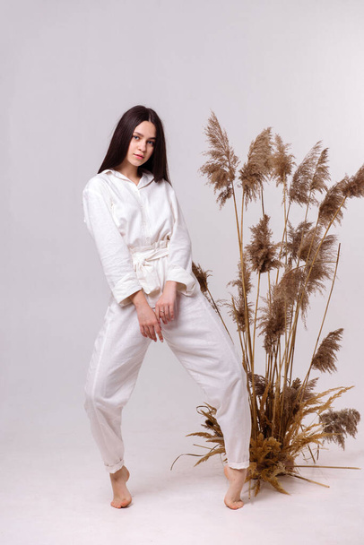 Hermosa chica en ropa ecológica natural blanca posando sobre un fondo claro. Concepto de ropa ecológica - Foto, Imagen