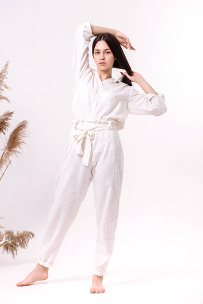 Beautiful girl in white natural eco clothes posing on a light background. Eco friendly clothes concept - 写真・画像
