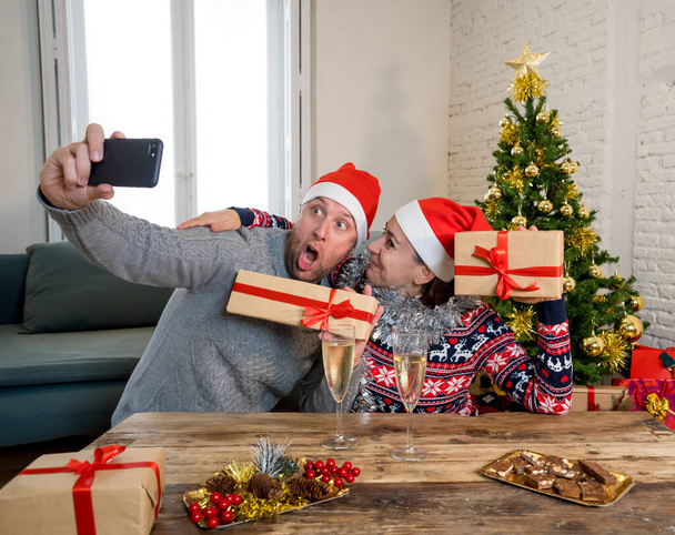 Ευτυχισμένο ζευγάρι βίντεο καλώντας φίλους με κινητό τηλέφωνο γιορτάζει Εικονικά Χριστούγεννα και το νέο έτος στο κλείδωμα. Εικονικοί εορτασμοί, κοινωνική απόσταση κατά τη διάρκεια των χειμερινών διακοπών λόγω COVID-19. - Φωτογραφία, εικόνα