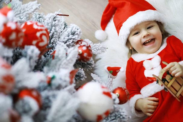 Merry bright christmas. Lovely baby enjoy christmas. Childhood memories. Santa girl little child celebrate christmas at home. Family holiday. Girl cute child cheerful mood play near christmas tree. - Photo, Image