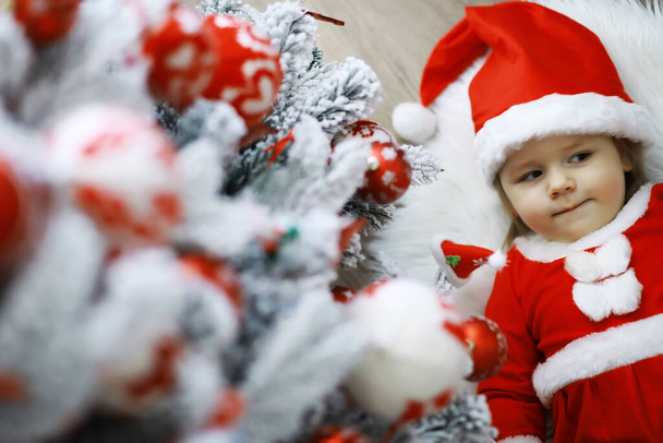 Veselé a veselé Vánoce. Krásné dítě si užije Vánoce. Dětské vzpomínky. Santa Girl malé dítě slaví Vánoce doma. Rodinná dovolená. Dívka roztomilé dítě veselá nálada hrát poblíž vánoční strom. - Fotografie, Obrázek