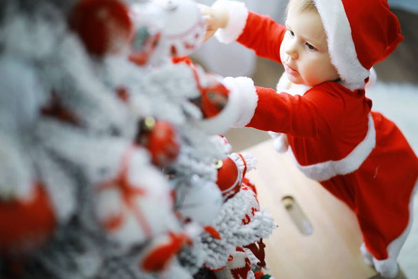 メリー・ブライト・クリスマス。素敵な赤ちゃんはクリスマスをお楽しみください。子供の頃の記憶。サンタの女の子の子供は自宅でクリスマスを祝います。家族の休日。女の子かわいい子供陽気な気分遊び近くクリスマスツリー. - 写真・画像