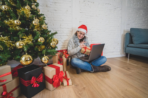 Happy woman alone in lockdown celebrating virtual christmas video calling family and friend. Virtual holiday gathering online due to coronavirus quarantine, social distancing and new restrictions. - 写真・画像