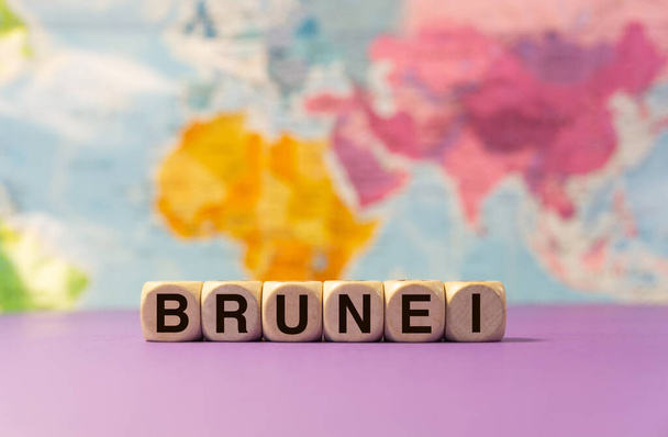 La palabra Brunei escrita con dados de madera delante de un fondo púrpura y un mapa geográfico - Foto, Imagen
