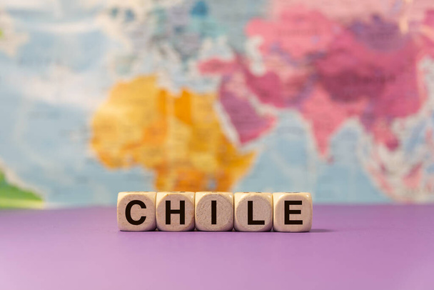 The word Chile written with wooden dices in front of a purple background and a geographic map - Photo, Image