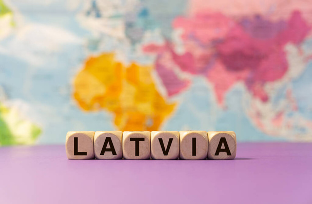 Slovo Lotyšsko napsané dřevěnými kostkami před purpurovým pozadím a zeměpisnou mapou - Fotografie, Obrázek