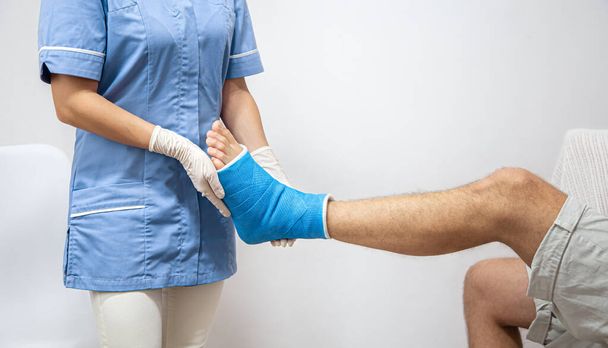 Acercamiento de la pierna de un hombre en un yeso y una férula azul después de vendar en un hospital. - Foto, Imagen
