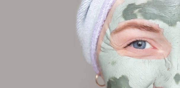 Μέρος του προσώπου μιας νεαρής γυναίκας με μια πήλινη μάσκα στο πρόσωπό της. Φροντίδα του δέρματος, θεραπείες ομορφιάς Spa. - Φωτογραφία, εικόνα