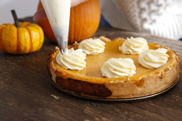 Traditional thanksgiving food on wooden table. Woman adding whipped topping to a delicious homemade pumpkin pie with crust. Top view, close up, copy space, background - Φωτογραφία, εικόνα