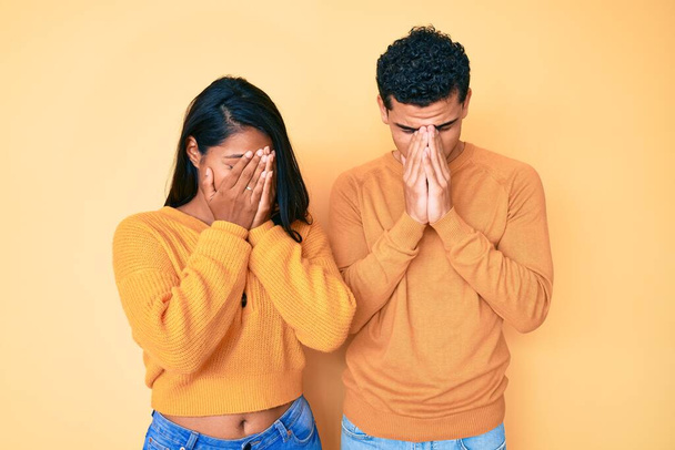 Beautiful latin young couple wearing casual clothes together with sad expression covering face with hands while crying. depression concept.  - Foto, Imagen