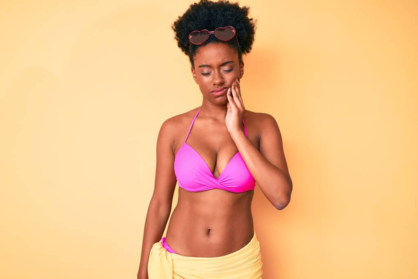 A fiatal afro-amerikai nő bikiniben fogdossa a száját, fájdalmas arckifejezéssel, fogfájás vagy fogbetegség miatt. fogorvos  - Fotó, kép