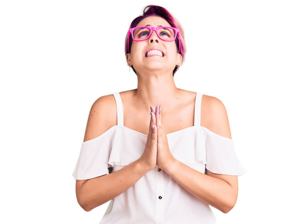 Young beautiful woman with pink hair wearing casual clothes and glasses begging and praying with hands together with hope expression on face very emotional and worried. begging.  - Photo, Image