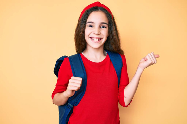Sevimli İspanyol çocuk sırt çantasını tutuyor gururla bağırıyor, zaferi kutluyor ve başarıyı kollarını kaldırarak kutluyor.  - Fotoğraf, Görsel
