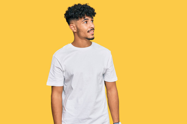 Mladý arabský muž v neformální bílé tričko, dívající se stranou s úsměvem na tváři, přirozený výraz. jistota smíchu.  - Fotografie, Obrázek