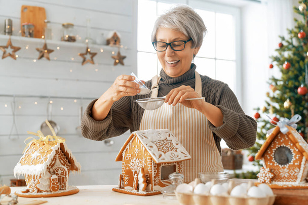 Merry Christmas and Happy Holidays. Family preparation holiday food. Woman cooking gingerbread house. - 写真・画像
