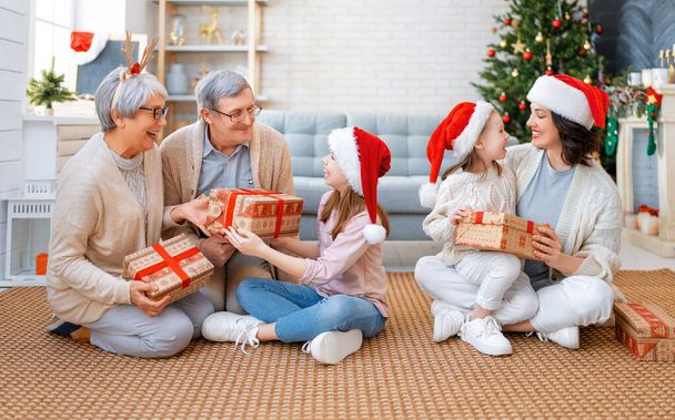 Merry Christmas and Happy Holidays! Grandma, grandpa, mum and children exchanging gifts. Parents and daughters having fun near tree indoors. Loving family with presents in room. - Fotoğraf, Görsel