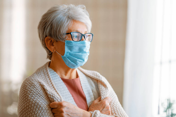 Starsza kobieta nosząca maskę twarzy podczas epidemii koronawirusu i grypy. Ochrona przed wirusami i chorobami, kwarantanna domowa. COVID-2019. Zdejmowanie lub zdejmowanie masek. - Zdjęcie, obraz