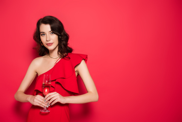 Brunette woman in dress holding glass of champagne on red background  - Foto, imagen