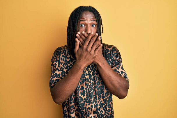Homme afro-américain avec des tresses portant une chemise léopard imprimé animal choqué couvrant la bouche avec les mains pour erreur. concept secret.  - Photo, image