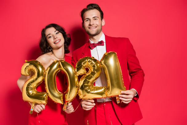 Cheerful couple holding balloons in shape of 2021 numbers on red background  - Photo, image