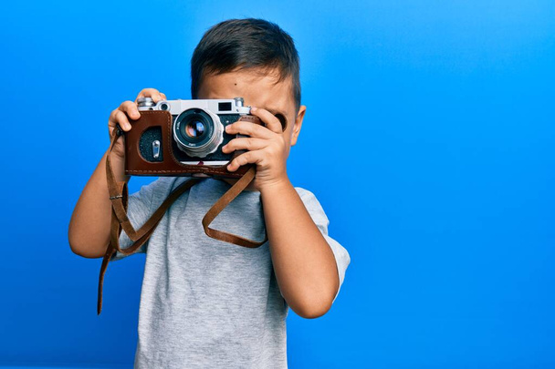 Entzückende lateinamerikanische Fotografin Kleinkind lächelt glücklich mit Vintage-Kamera über isolierten blauen Hintergrund. - Foto, Bild