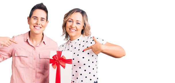 Пара жінок тримає подарунок, вказуючи пальцем на одного себе, усміхаючись щасливим і гордим
  - Фото, зображення