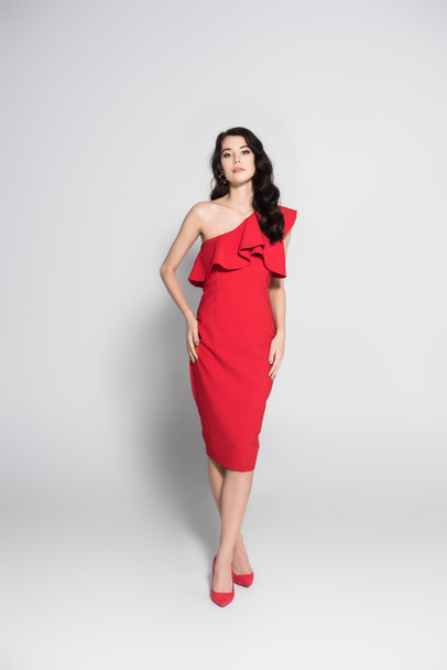 Stylish woman in red dress and heels looking at camera on grey background  - Фото, зображення