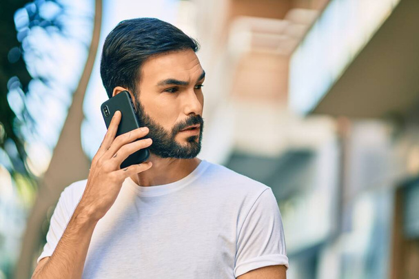 Joven hombre hispano con expresión seria hablando en el smartphone de la ciudad. - Foto, imagen