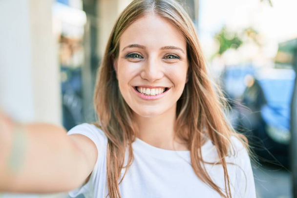 Mladá běloška žena se šťastně usmívá, aby selfie u kamery ve městě - Fotografie, Obrázek